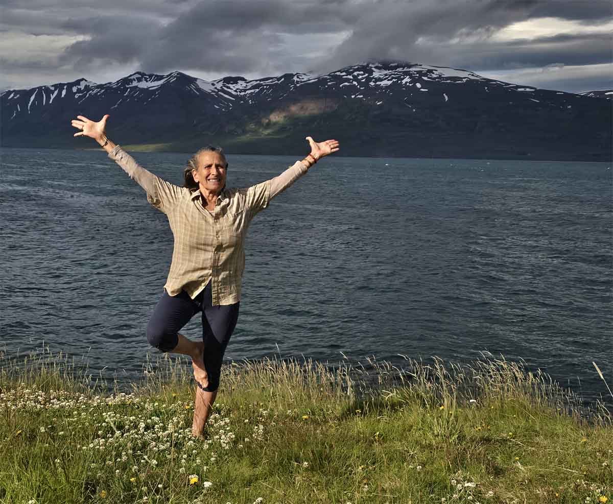 Ajeet in a yoga pose in Iceland with fjord and mountains behind